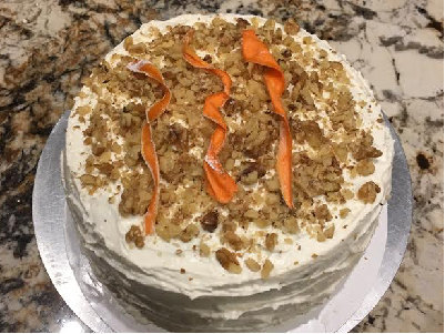 Carrot cake with white frosting, chopped nuts and carrot ribbons