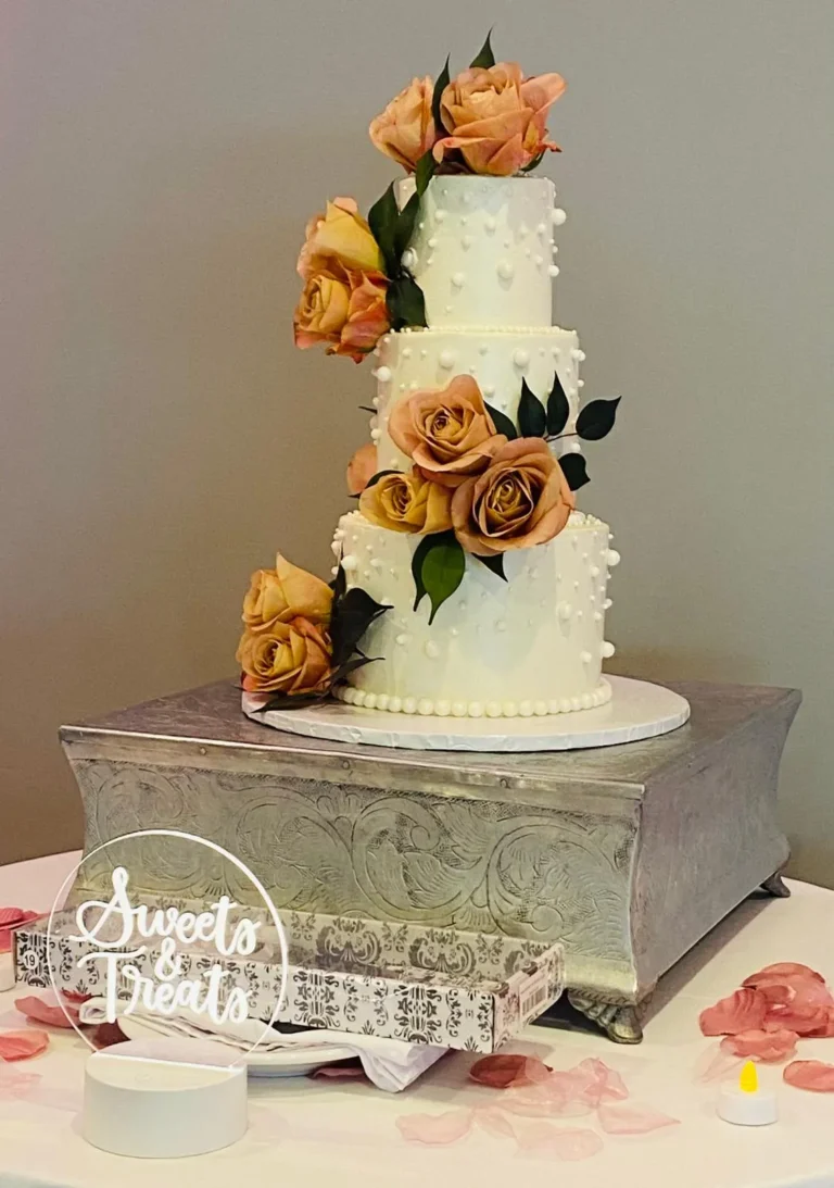 Four-tier white wedding cake with copper roses on a silver stand