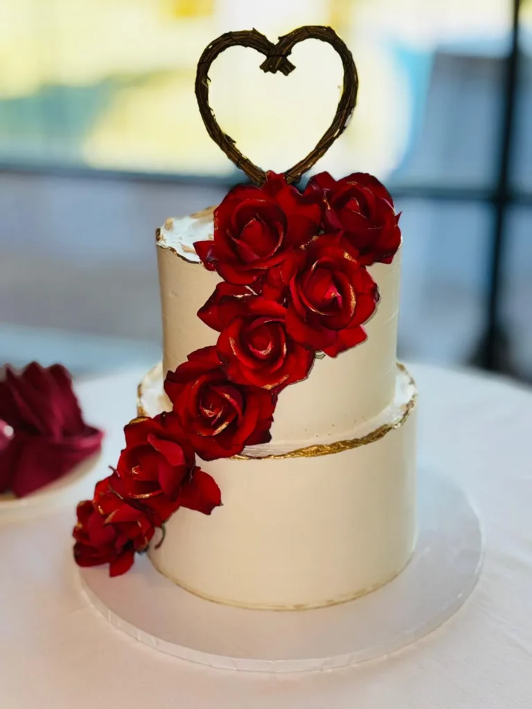 Two-tier wedding cake with a red rose cascade and a heart topper