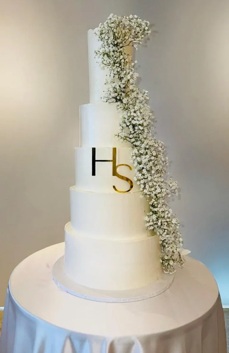 flans & cakes Tall four-tier white wedding cake with an H S monogram and baby's breath