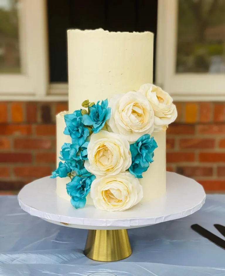Tall white cake with teal and ivory roses on a gold stand