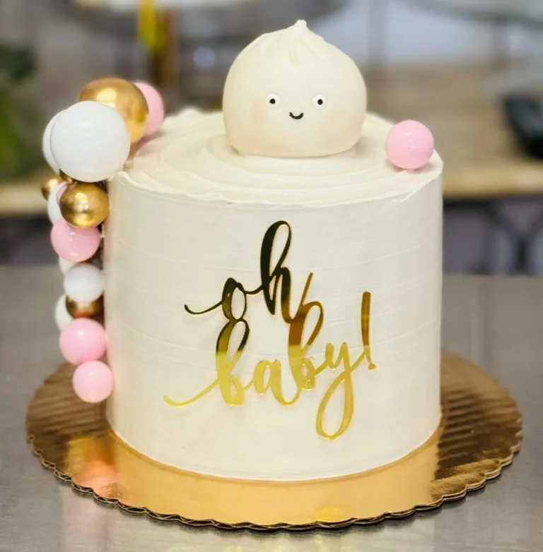 White baby shower cake with a smiling dumpling topper, an "Oh baby!" sign and pink and gold balls