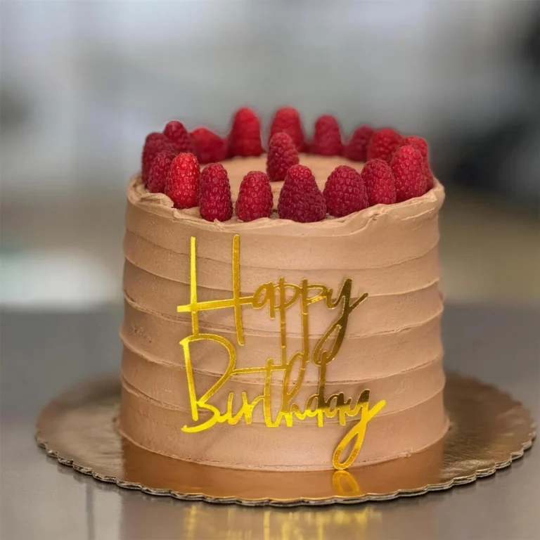 Chocolate buttercream birthday cake topped with fresh raspberries and a gold "Happy Birthday" sign