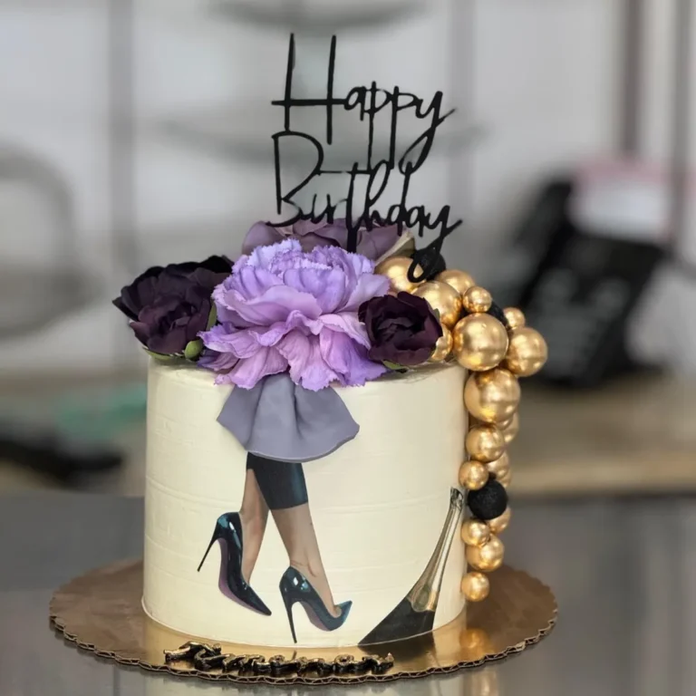 White birthday cake with a high-heels fashion design, purple flowers and gold balls
