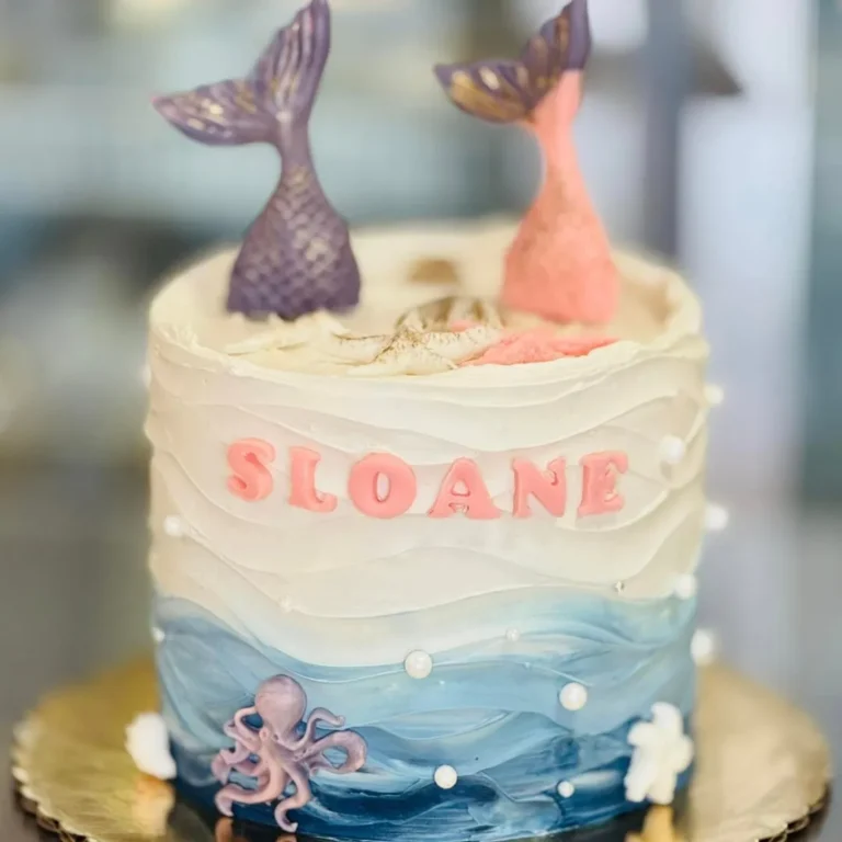 Ocean wave birthday cake with two mermaid tails, an octopus and the name Sloane