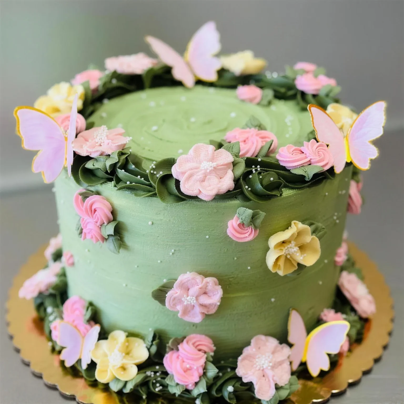 Sage green birthday cake with pink buttercream flowers and butterflies
