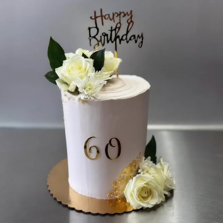 Tall white 60th birthday cake with white roses and a gold "Happy Birthday" topper