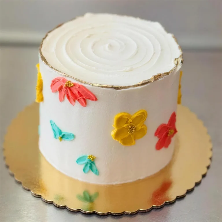 White cake with a gold rim and red, yellow and teal painted flowers